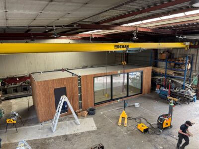 Modulaire unit van ROBCOR in aanbouw in de werkplaats, met houten structuur en een kraan boven het werkstuk.