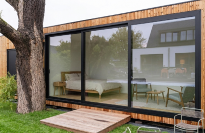 Modulair gastenverblijf of bijwoonst op maat in een Vlaamse tuin, met houten gevel en grote glazen schuifdeuren.
