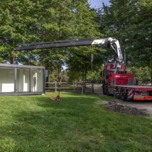 Rode kraan hijst een modulaire unit van ROBCOR op een groene locatie tijdens de plaatsing.
