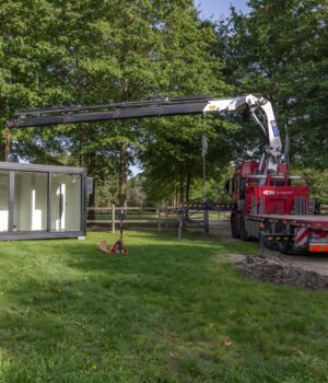 Rode kraan hijst een modulaire unit van ROBCOR op een groene locatie tijdens de plaatsing.