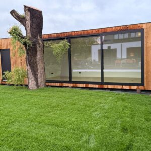 Tuinkantoor op maat van ROBCOR met houten gevel en grote zwarte raampartijen in de tuin.