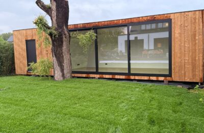 Tuinkantoor op maat van ROBCOR met houten gevel en grote zwarte raampartijen in de tuin.