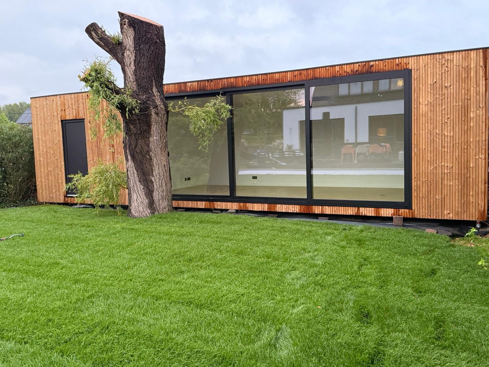 Tuinkantoor op maat van ROBCOR met houten gevel en grote zwarte raampartijen in de tuin.