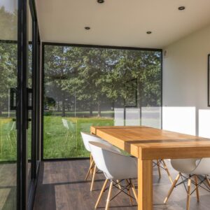 Modulaire woonunit op maat van ROBCOR met grote glaspartijen, houten eettafel en lichte leefruimte.
