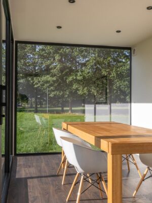 Modulaire woonunit op maat van ROBCOR met grote glaspartijen, houten eettafel en lichte leefruimte.
