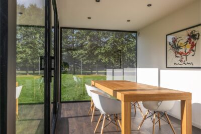 Modulaire woonunit op maat van ROBCOR met grote glaspartijen, houten eettafel en lichte leefruimte.