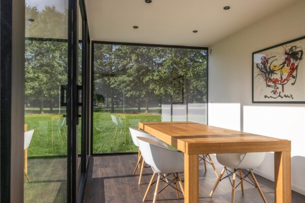 Modulaire woonunit op maat van ROBCOR met grote glaspartijen, houten eettafel en lichte leefruimte.