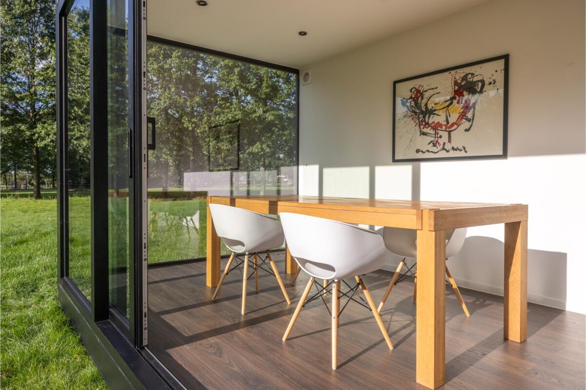Lichte leefruimte in een modulaire woonunit van ROBCOR met eettafel, witte stoelen en grote ramen.